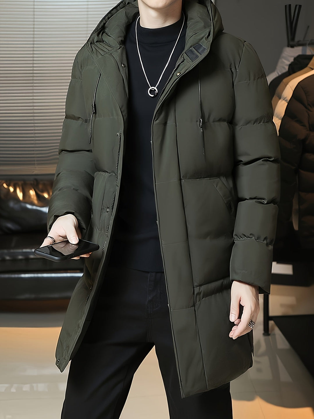 Man wearing Barnaby green puffer coat with hood up, holding phone