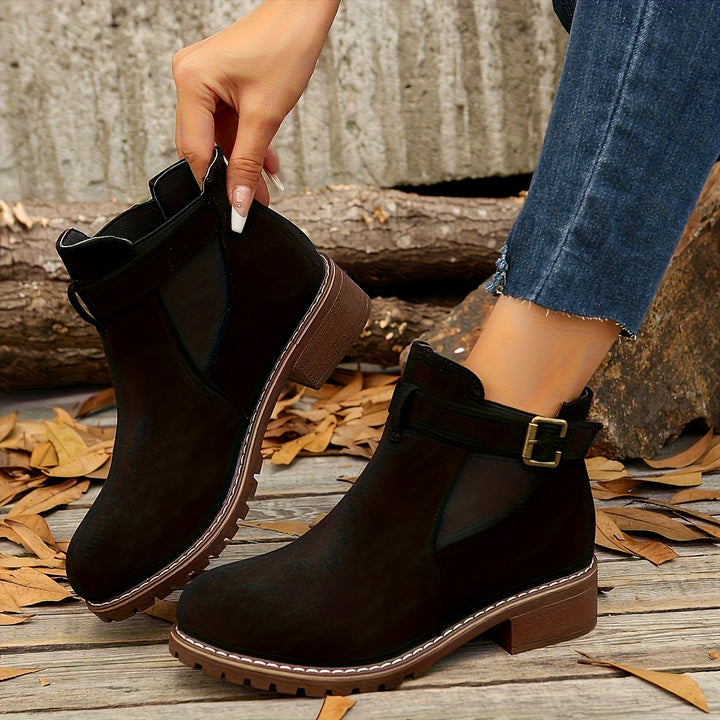 Marigold buckle strap Chelsea boots in black, held by hand