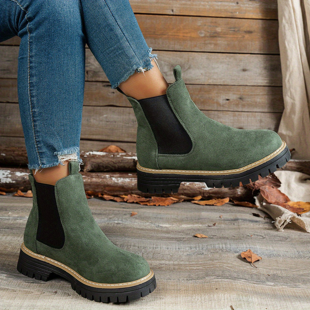 Green Chelsea boots worn with ripped denim jeans, side view