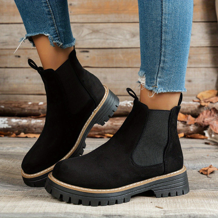 Black Chelsea boots worn with ripped denim jeans, side view