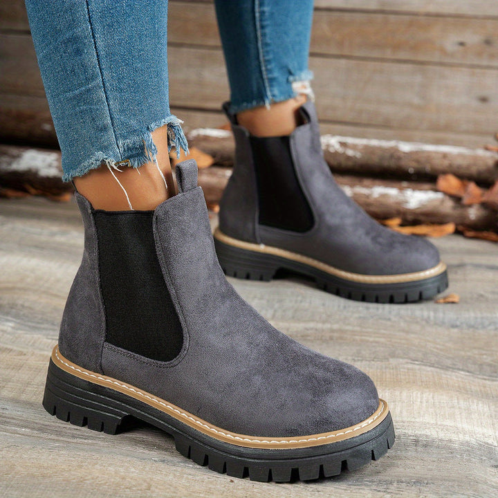 Grey Chelsea boots worn with ripped denim jeans, walking pose